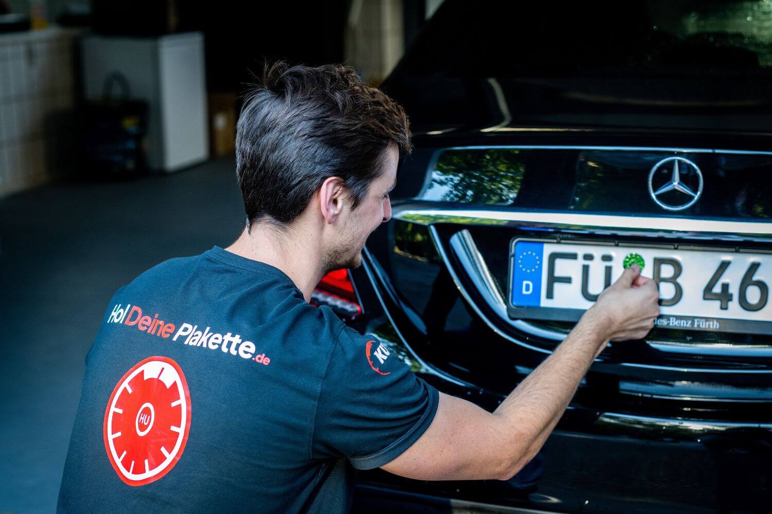 Ein Mann klebt in einer Fürther Hauptuntersuchungsstelle eine Plakette auf das Nummernschild